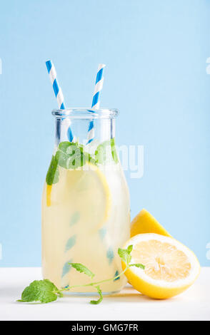 Bottiglia di limonata fatta in casa con la menta, ghiaccio, limoni, carta cannucce e pastello sfondo blu Foto Stock