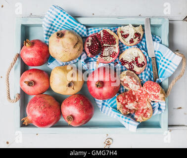 Il bianco e il rosso melograno con un coltello da cucina asciugamano in blu il vassoio sulla luce dipinta sullo sfondo di legno Foto Stock