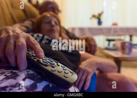 Anziana coppia anziana che si trova a casa rilassarsi su un divano in un soggiorno guardando la TV. Coronavirus COVID19 blocco pandemico. Tutti i giorni. Foto Stock