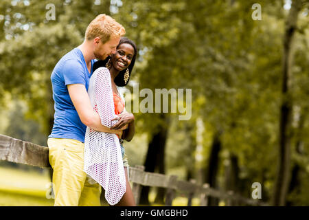 Giovane coppia multirazziale in amore in piedi accanto al recinto nel parco in una giornata di sole Foto Stock