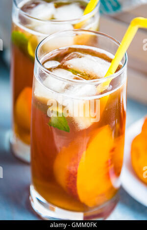 Con occhiali in casa ice tea, peach aromatizzato. Appena tagliate fette di pesche per la disposizione. La luce blu sullo sfondo di legno. Foto Stock