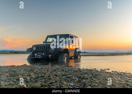 Jeep 4x4 contro il tramonto. Jeep è rimasto bloccato nel fango. Foto Stock