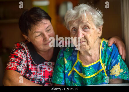 Triste donna anziana, in background abbracciando figlia adulta. Foto Stock