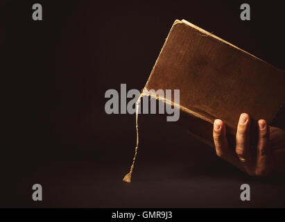 Composizione concettuale, mano d'uomo in possesso di un vecchio libro aperto. Foto Stock