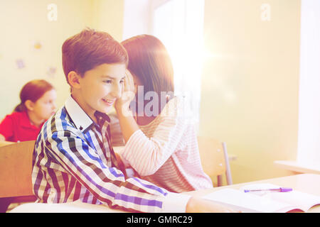 Sorridente schoolgirl whispering a classmate orecchio Foto Stock