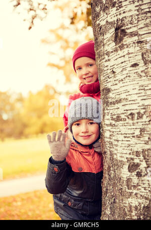 Dei bambini felici di nascondersi dietro ad albero e agitando la mano Foto Stock