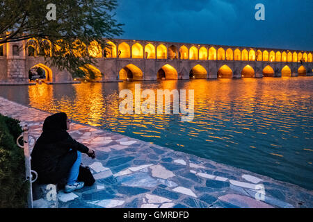 Donna iraniana in hijab guardando il Allāhverdi Khan Bridge popolarmente noto come si-o-seh pol "ponte di trenta-tre campate", una delle undici ponti di Isfahan, Iran e il più lungo ponte sul fiume Zayandeh con la lunghezza totale di 297.76 metri (976.9 ft). È altamente classificato come uno dei più famosi esempi di Safavid bridge design. Foto Stock