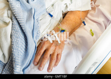 IV in mano di Senior paziente di sesso maschile che giace in un letto di ospedale. Stretta di mano e braccio. Foto Stock