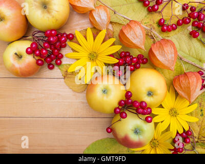 Mele, fiori gialli, physalis lanterne, bacche e foglie di autunno su tavole di legno sfondo Foto Stock