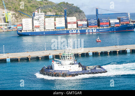 Un grande rimorchiatore lungo un enorme, caricato CMA CGM freighter in St Maarten Foto Stock