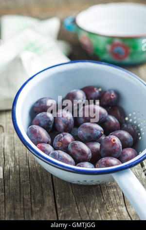 Prugne fresche da giardino in scolapasta sul vecchio tavolo in legno. Foto Stock