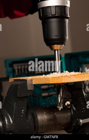 Immagine del foro di trivellazione con il cacciavite nel pezzo di legno bloccato nella morsa. Foto Stock