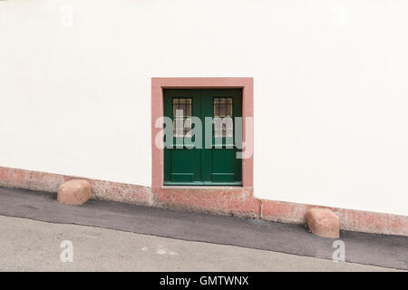 Un muro bianco con una piccola porta verde e rosa cornice colorata si trova nel mezzo. Foto Stock