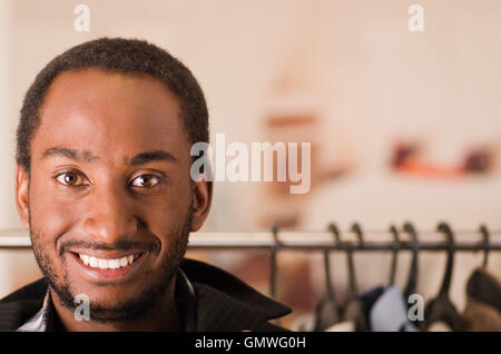 Headshot giovane uomo sorridente alla telecamera, in piedi nella parte anteriore del rack di abbigliamento, fashion concept Foto Stock