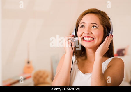 Giovane donna indossa top bianco e la cuffia di fronte alla fotocamera mentre interagiscono sorridente, hanno sottolineato il concetto Foto Stock