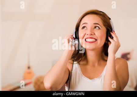 Giovane donna indossa top bianco e la cuffia di fronte alla fotocamera mentre interagiscono sorridente, hanno sottolineato il concetto Foto Stock