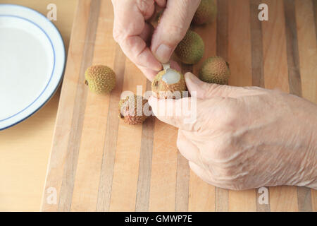 Un uomo inizia a sbucciare un fresco litchi su un tagliere. Foto Stock