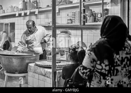 Folla in attesa fuori faloodeh popolare negozio per il dolce a base di noodle dessert in Yazd, Iran. Bianco e Nero notte scena di strada. Foto Stock