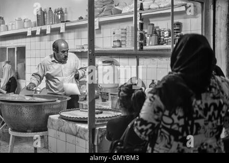 Folla in attesa fuori faloodeh popolare negozio per il dolce a base di noodle dessert in Yazd, Iran. Notte street scene in bianco e nero. Foto Stock