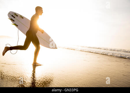 Un surfista con la sua tavola da surf in esecuzione per le onde Foto Stock