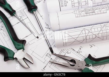 Rotoli di diagrammi, metallo una pinza e un cacciavite elettrico sul disegno di costruzione della casa, accessori per progetti engineer j Foto Stock