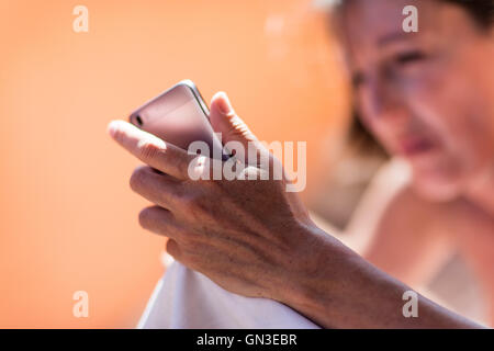 La mano di una donna che mantiene uno smartphone con un età e pelle chiazzato Foto Stock