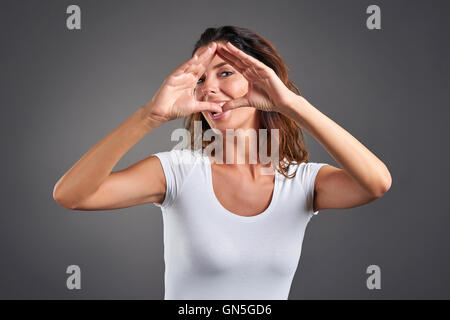 Una giovane e bella donna sagomatura di un triangolo con le sue mani e guardando attraverso di esso. Foto Stock