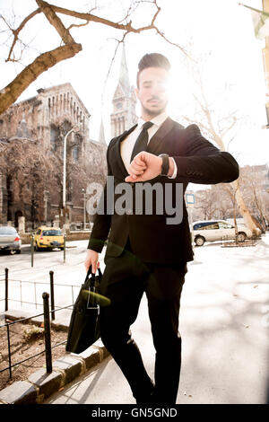 Giovane uomo a camminare sulla strada, controllo del tempo sul suo orologio da polso Foto Stock
