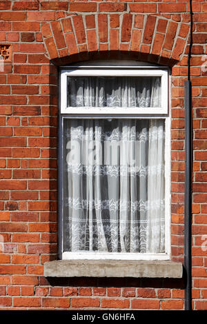 Vecchio net curtains appeso nella finestra di un mattone rosso vittoriano casa a schiera Foto Stock