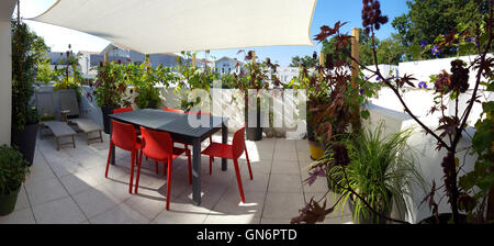 La terrazza di un appartamento arredato con un set di mobili da giardino, sedie a sdraio e una vela di ombra. La terrazza sul tetto. Appartamento terrazza superiore. Foto Stock