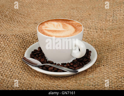 Cappuccino con chicchi di caffè su sfondo di iuta Foto Stock