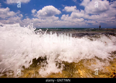 Pescatore solitario con la bassa marea su una spiaggia in un'onda si rompe sulla riva in primo piano Foto Stock