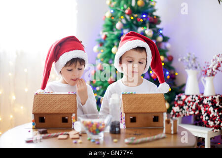 Due ragazzi dolce, fratelli, rendendo gingerbread cookies house, la decorazione a casa nella parte anteriore dell'albero di Natale, bambini che giocano e Foto Stock