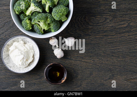 Una ciotola con broccoli freschi, i chiodi di garofano di aglio, formaggio Filadelfia e olio d'oliva sul legno scuro dello sfondo. Zuppa di Brocoli ingredie Foto Stock