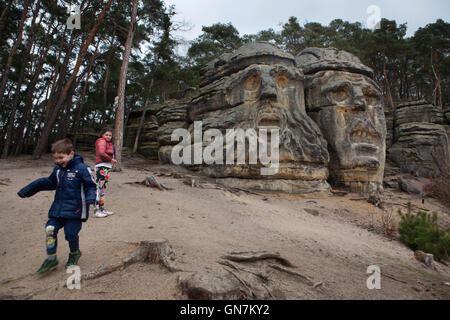 I bambini giocano accanto al diavolo i capi scolpiti da scultore ceco Vaclav Levy nelle rocce di arenaria nella foresta appena fuori dal villaggio di Zelizy nella Boemia centrale, Repubblica Ceca. Due grandi capi sono stati creati da Vaclav prelievo durante il 1840s insieme con il Klacelka Grotta e la Harfenice (arpista) situato nella foresta vicino a. Foto Stock