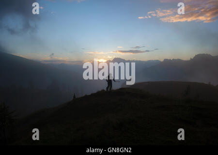 Le Dolomiti, Trentino, Italia settentrionale. Sunrise oltre le montagne si vede dal Passo di Valles con un allevatore locale Foto Stock