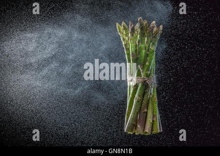 Asparagi in schizzi su sfondo nero. Close-up. Una serie di frutta e verdura in movimento. Foto Stock