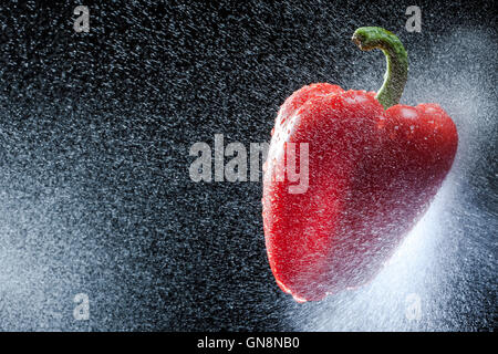 Peperone rosso in uno spray contro uno sfondo nero. Una serie di frutta e verdura in movimento. Foto Stock