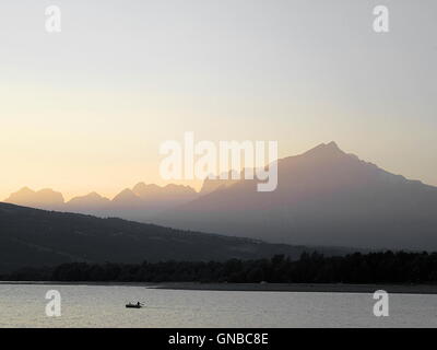 Full frame shot del tramonto con le montagne, il lago, la foresta e la piccola barca Foto Stock