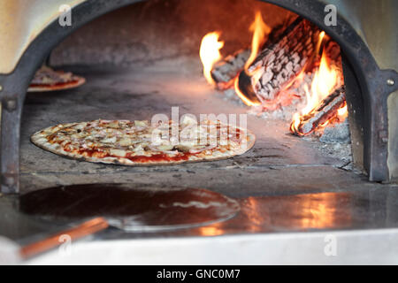 Uomo di mettere appena fatta la pizza in forno a legna per la pizza Foto Stock