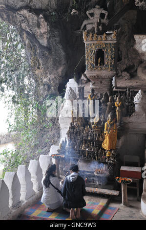 Pak Ou Grotta, giovane pregando davanti di statue di Buddha Foto Stock