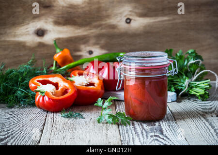 In casa i peperoncini sott'aceto nel succo di pomodoro e campana dolce peperone rosso sul tavolo rustico Foto Stock