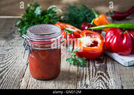 In casa i peperoncini sott'aceto nel succo di pomodoro e campana dolce peperone rosso sul tavolo rustico Foto Stock