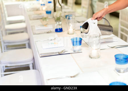 Donna versando acqua da stanless jar per un bicchiere Foto Stock