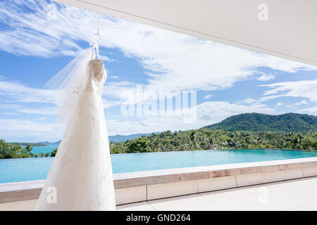 White abito da sposa appeso su una delle spalle, bel cielo azzurro sfondo. Foto Stock