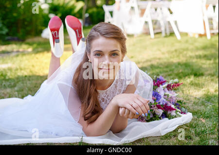 Sposa giacente sull'erba nel giardino di primavera Foto Stock