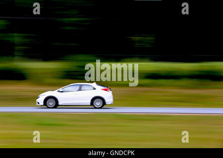 Piccola vettura bianca ad alta velocità in autostrada, panning tecnica, spazio copia a destra. Foto Stock