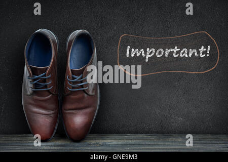 Importante testo sulla lavagna nera e business scarpe sul pavimento in legno Foto Stock