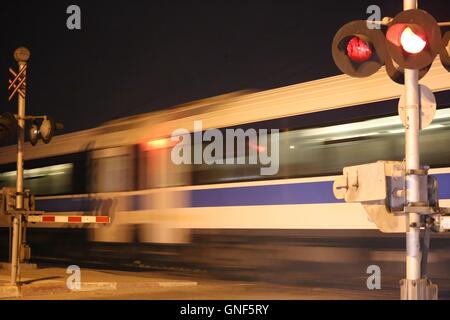 Il treno passa Railroad Crossing. Un treno che passa in velocità attraverso un passaggio a livello di notte. Incrocio ferroviario (attraversamento ferroviario) con accelerazione passeng Foto Stock