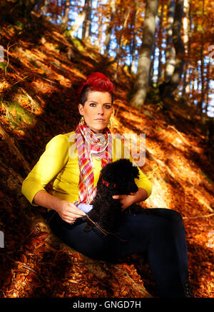 Carina ragazza con cane nero sorridente e abbracciando presso la foresta di autunno all'esterno. Foto Stock